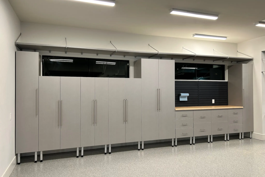 Garage with custom storage cabinets, overhead shelving, workbench, slat wall, and durable polyaspartic flooring