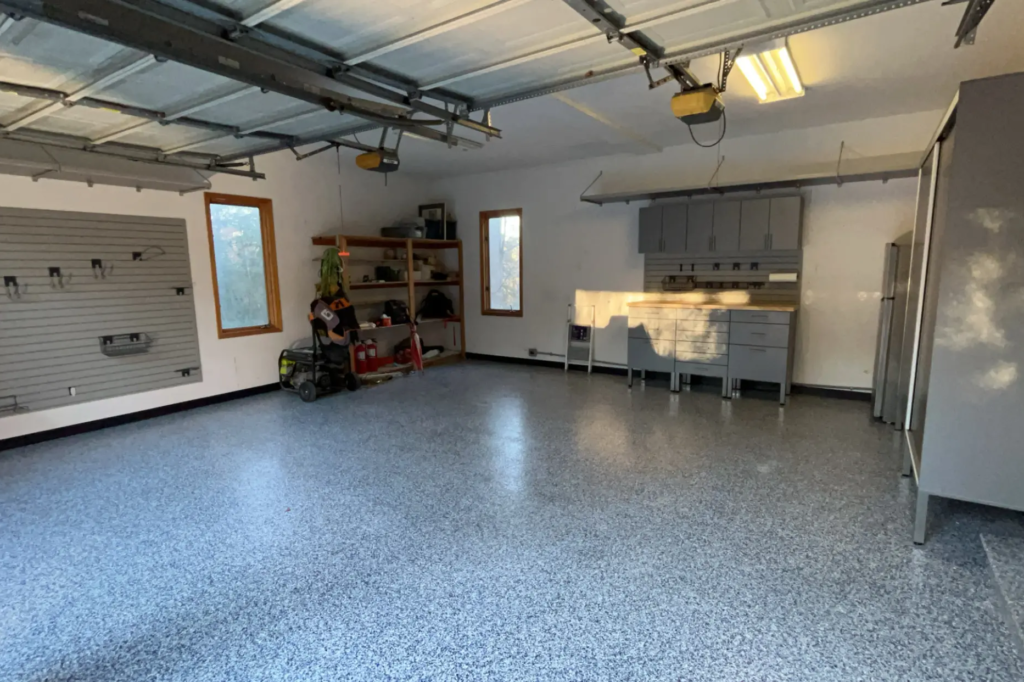 Spacious garage with polyaspartic flooring, slat wall storage, custom workbench, and overhead shelving