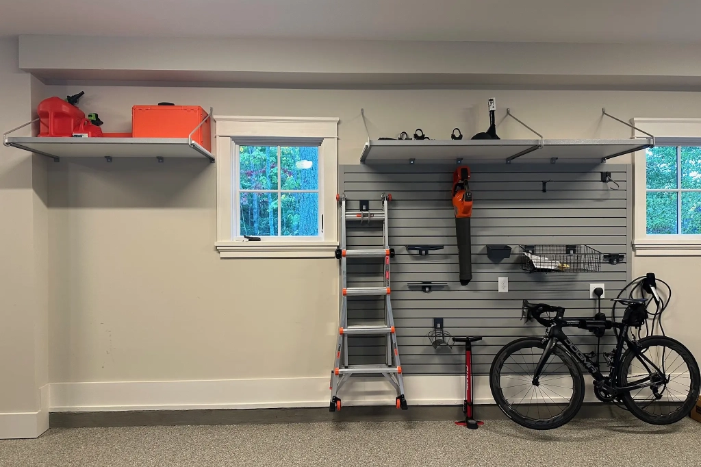 Garage with slat wall storage system, overhead shelving, and polyaspartic flooring for optimized organization